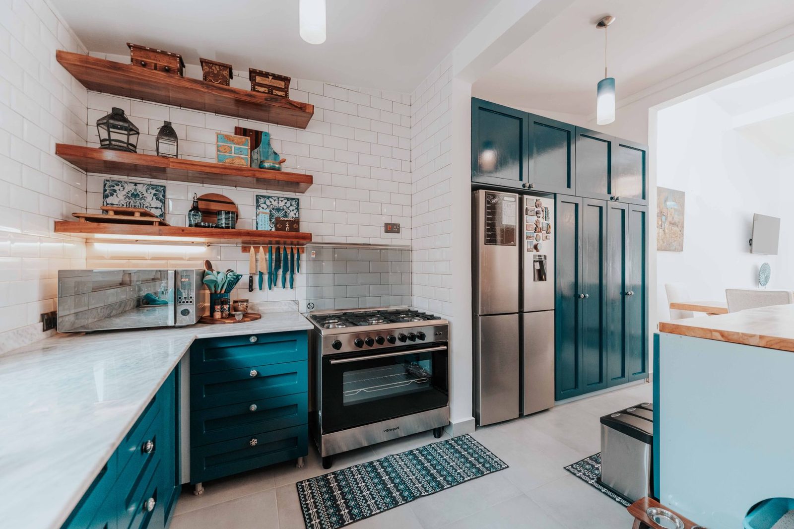 A kitchen with deep teal cabinets, white subway tile and open wooden shelving