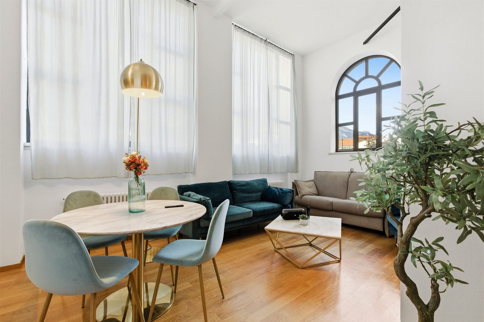 A bright living and dining space with a blue sofa and arched windows