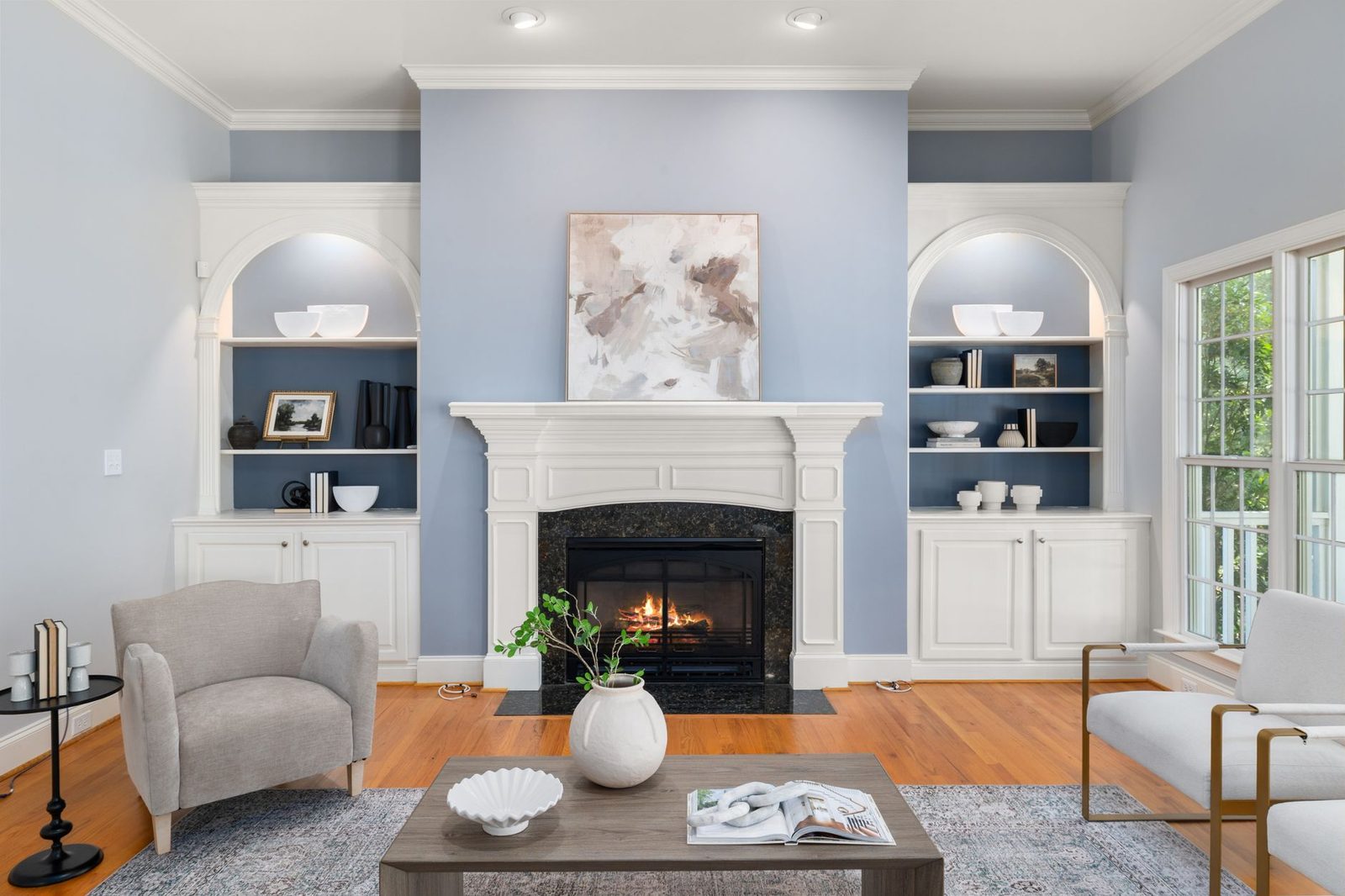 A pale blue living room with white built-in shelving either side of a fireplace