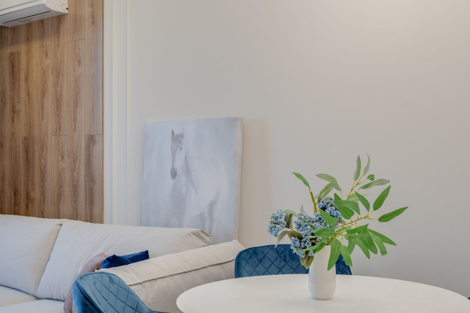 A bright living room with a white sofa, blue cushions and a large plant