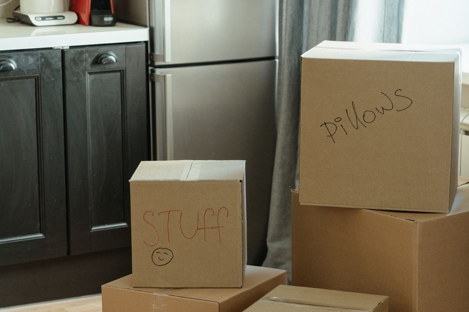 Moving boxes stacked in a kitchen beside the fridge in a newly occupied house