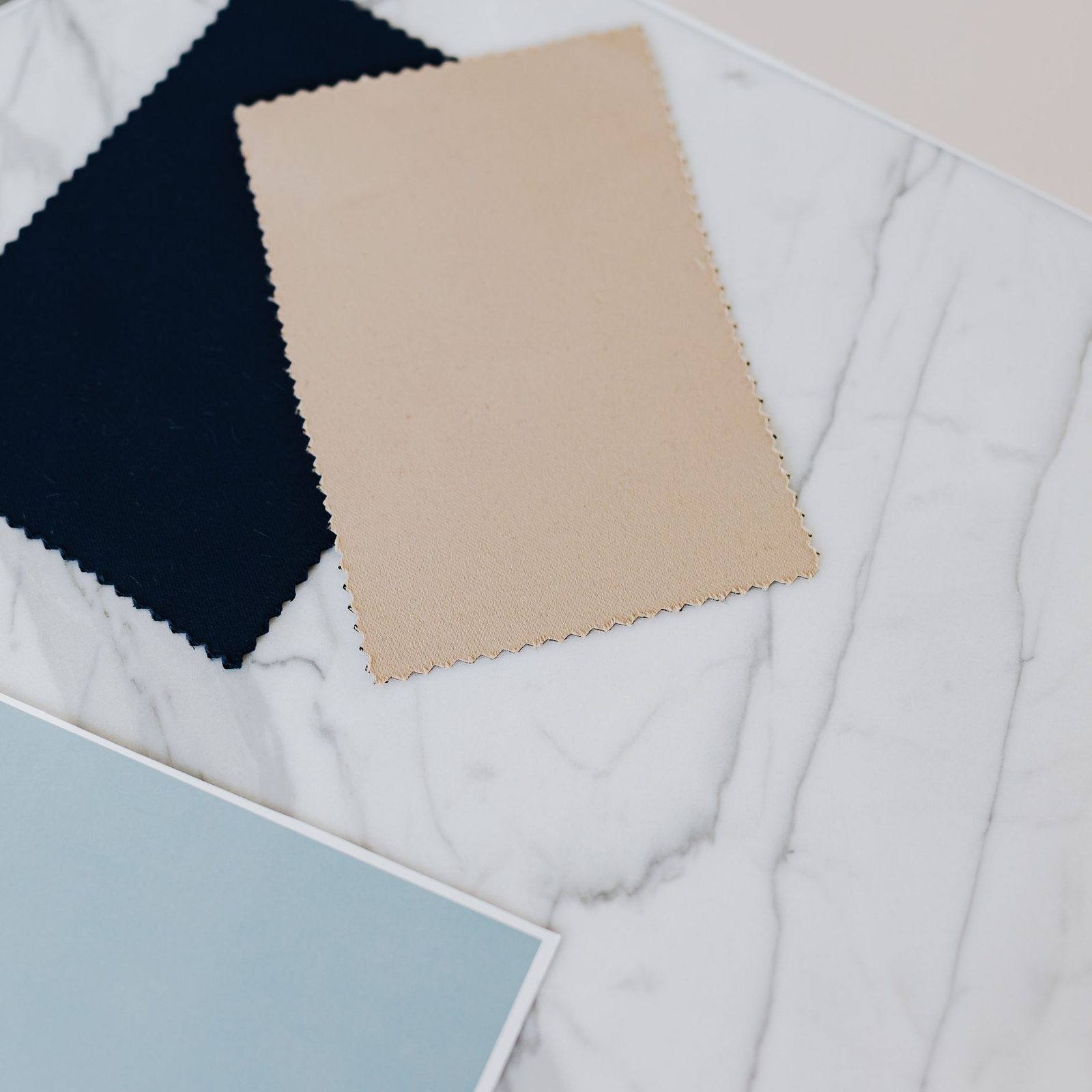 Navy, tan and pale blue fabric swatches laid on a marble surface