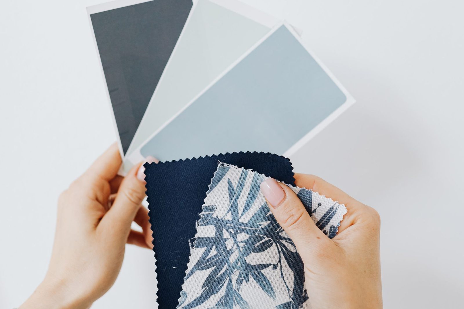 Hands laying blue paint chips and a patterned fabric sample on a table